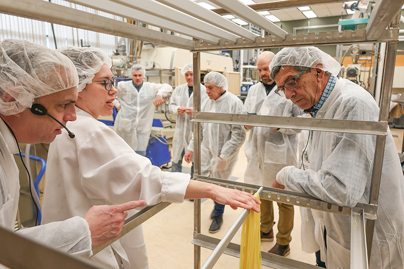A group of participants watch a Cereals Canada pasta expert place fresh spaghetti on a drying rack. A group of participants watch a Cereals Canada pasta expert place fresh spaghetti on a drying rack.